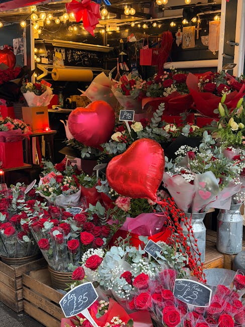 A vibrant display of floral arrangements in a flower shop, featuring red roses, white flowers, and green foliage, wrapped in pink and red tissue paper, with two heart-shaped red balloons visible among